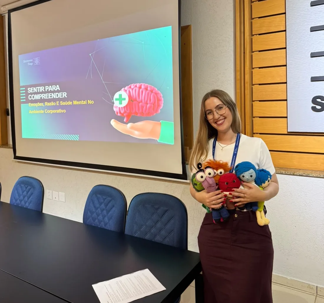 Laleska segurando bonecos de crochê de emoções ao lado do slide da palestra Sentir para Compreender